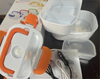 White and orange electric lunchbox with multiple compartments, shown with its packaging box, accessories including a car charger and spoon, and a clear plastic container on a dark surface.
